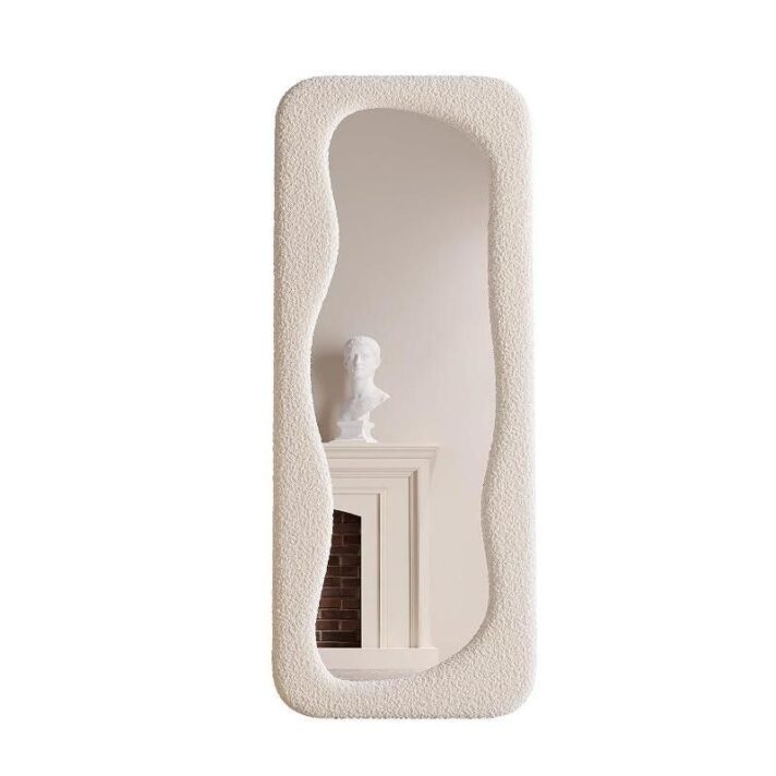 Cream textured full-length mirror with an irregular wavy frame, reflecting a neutral interior with a mantel and bust sculpture, showcasing a tall elegant silhouette
