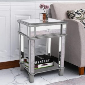 Silver mirrored bedside table with a glass top and drawer, featuring a crystal-style handle, open shelf below, and chrome-finished frame, placed beside a beige sofa. Brand: Verra Luxe Home product: Silver Mirrored Bedside Table with Drawer & Open Shelf