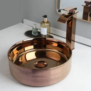 Copper-toned round vessel sink with a glossy metallic finish, paired with a modern waterfall faucet and complementary bathroom countertop accessories, showcased by Verra Luxe Home
