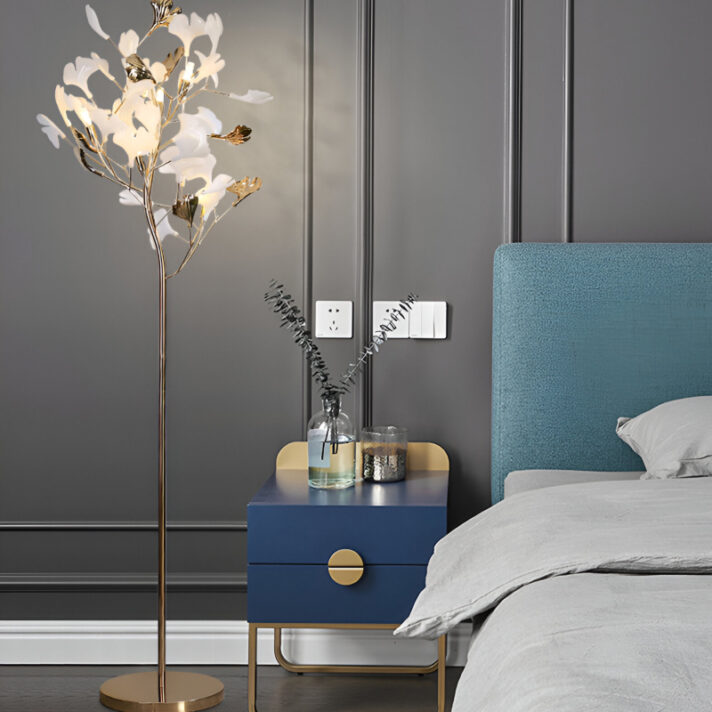 Nordic Ginkgo Leaf LED Floor Lamp with metallic finish stands beside a blue nightstand in a modern bedroom, featuring ambient LED light and a minimal, nature-inspired silhouette.