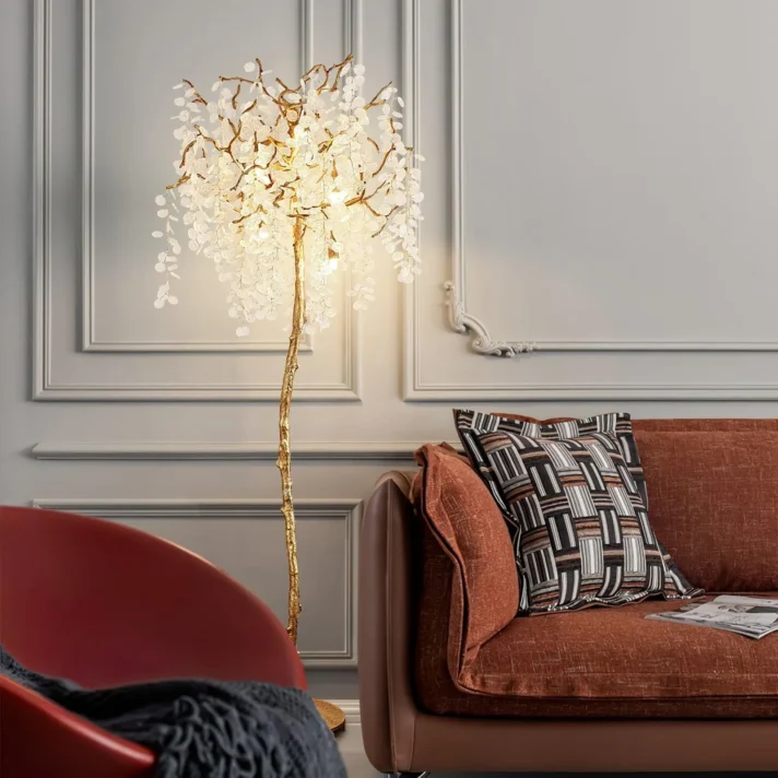 Verra Luxe Home Luxury Crystal Tree Floor Lamp with a golden stem and crystal branches, illuminated in a modern living room beside a rust-colored sofa.
