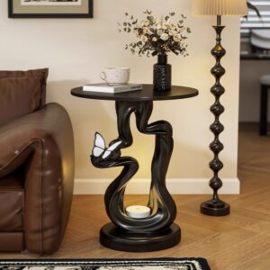 Verra Luxe Home Modern Retro Resin Side Table with a black sculptural curved base and round top, featuring a butterfly accent, candle, and floral vase.