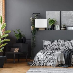58" Matte Black Floor Lamp with a White Linen Shade stands tall in a dark grey bedroom, featuring a minimalist Nordic design, tall curved arm, lush green plants, and monochrome bedding for a chic, modern vibe.