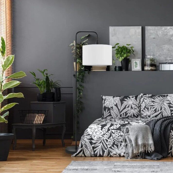 58" Matte Black Floor Lamp with a White Linen Shade stands tall in a dark grey bedroom, featuring a minimalist Nordic design, tall curved arm, lush green plants, and monochrome bedding for a chic, modern vibe.