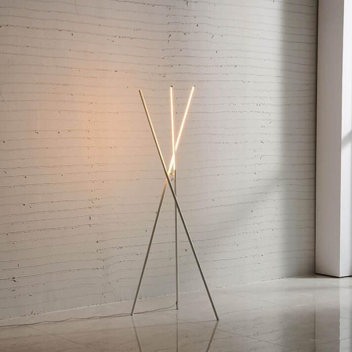 Modern Nordic LED Floor Lamp in aluminum with a minimalist three-pronged frame, crossing legs and emitting a warm upward glow, by Verra Luxe Home.