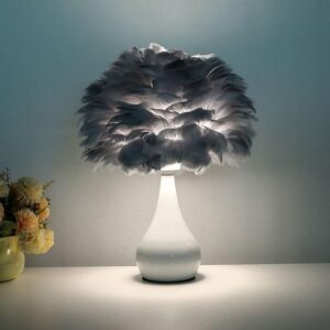 Chic White Feather LED Table Lamp with a curved white ceramic base and a large soft gray feather lampshade, softly lit on a minimalist surface.
