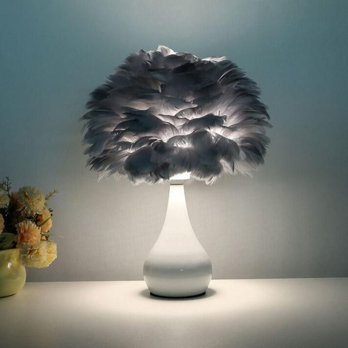 Chic White Feather LED Table Lamp with a curved white ceramic base and a large soft gray feather lampshade, softly lit on a minimalist surface.