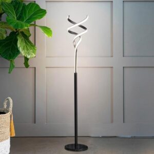 Modern black floor lamp with a sculptural silver spiral LED head stands beside a green plant against a grey paneled wall, showcasing contemporary minimalist lighting.
