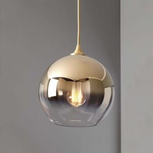 Gold pendant light with a spherical glossy glass globe and brass cord, reflecting a modern gray interior with warm glow.