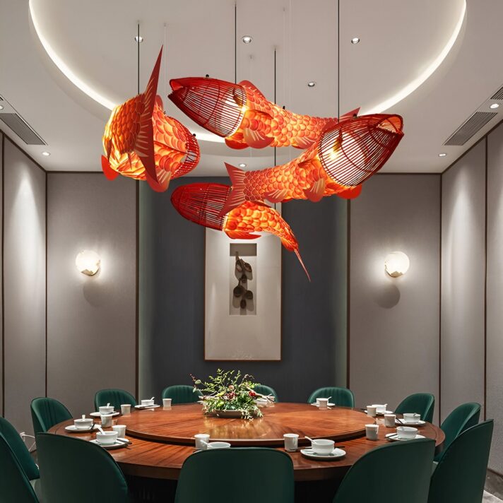 Red fish-shaped lanterns suspended over a round wooden dining table in a modern dining room with green upholstered chairs and soft wall lighting.