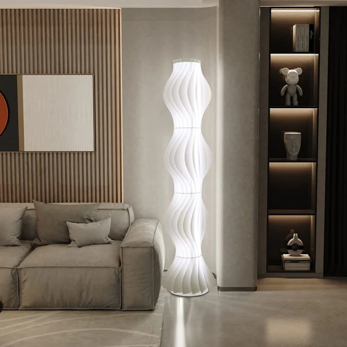 White sculptural spiral floor lamp in a modern Verra Luxe Home living room, placed beside a gray sofa and a built-in shelving unit with ambient lighting.