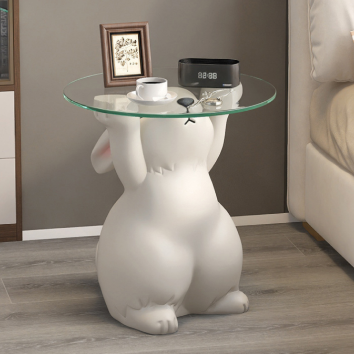 White rabbit statue side table with a round glass top, glossy resin finish, and a small framed art piece on the tabletop in a modern living room setting