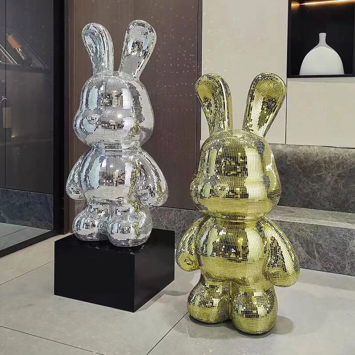 A pair of glossy disco bunny statues in silver and gold finishes, reflecting light on a modern showroom floor, two oversized rabbit figures