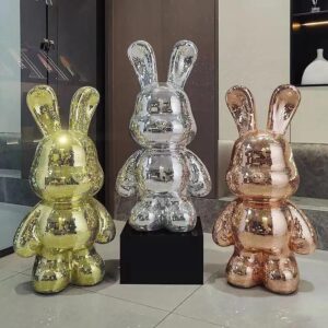 Three mosaic rabbit statues in gold, silver, and bronze finishes with mirrored tiles, reflecting a modern luxury vibe in a showroom setting
