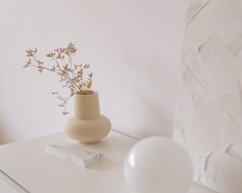 Beige ceramic vase with a dried sprig on a white surface in a minimalist Nordic-inspired decor scene, highlighting Scandinavian design elements